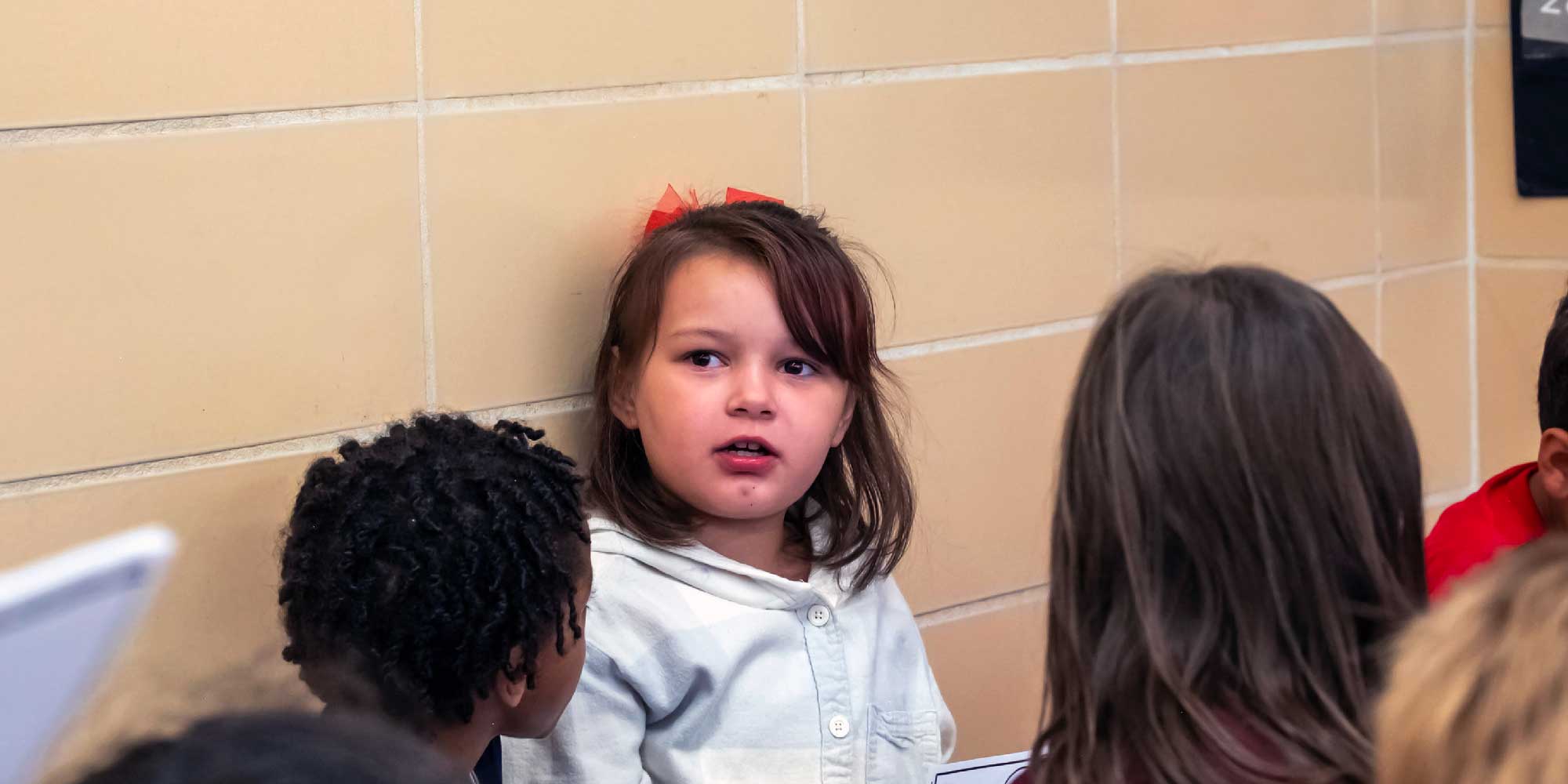 Student with a red bow in her hair listening attentively in class.