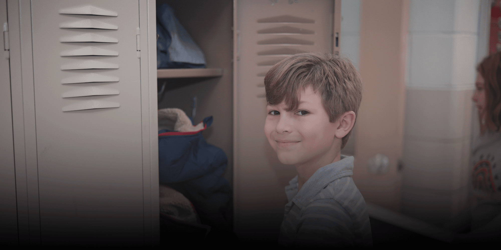 Smiling student standing in front of an open school locker.